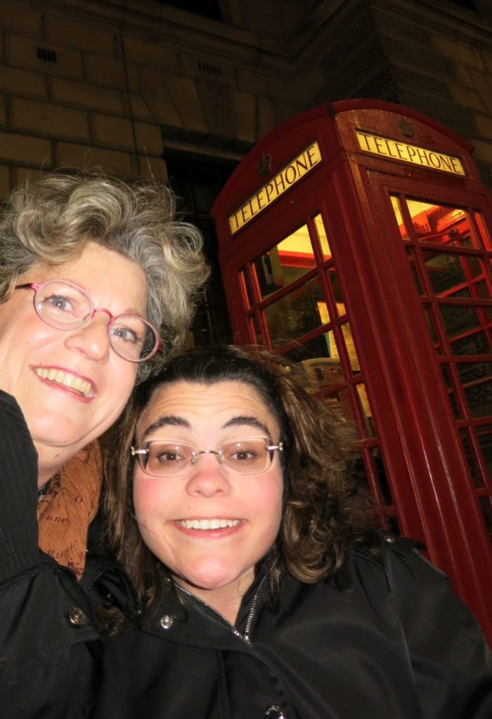alt text=Nadia and her mom who is her caregiver in front of a red English  Telephone booth.